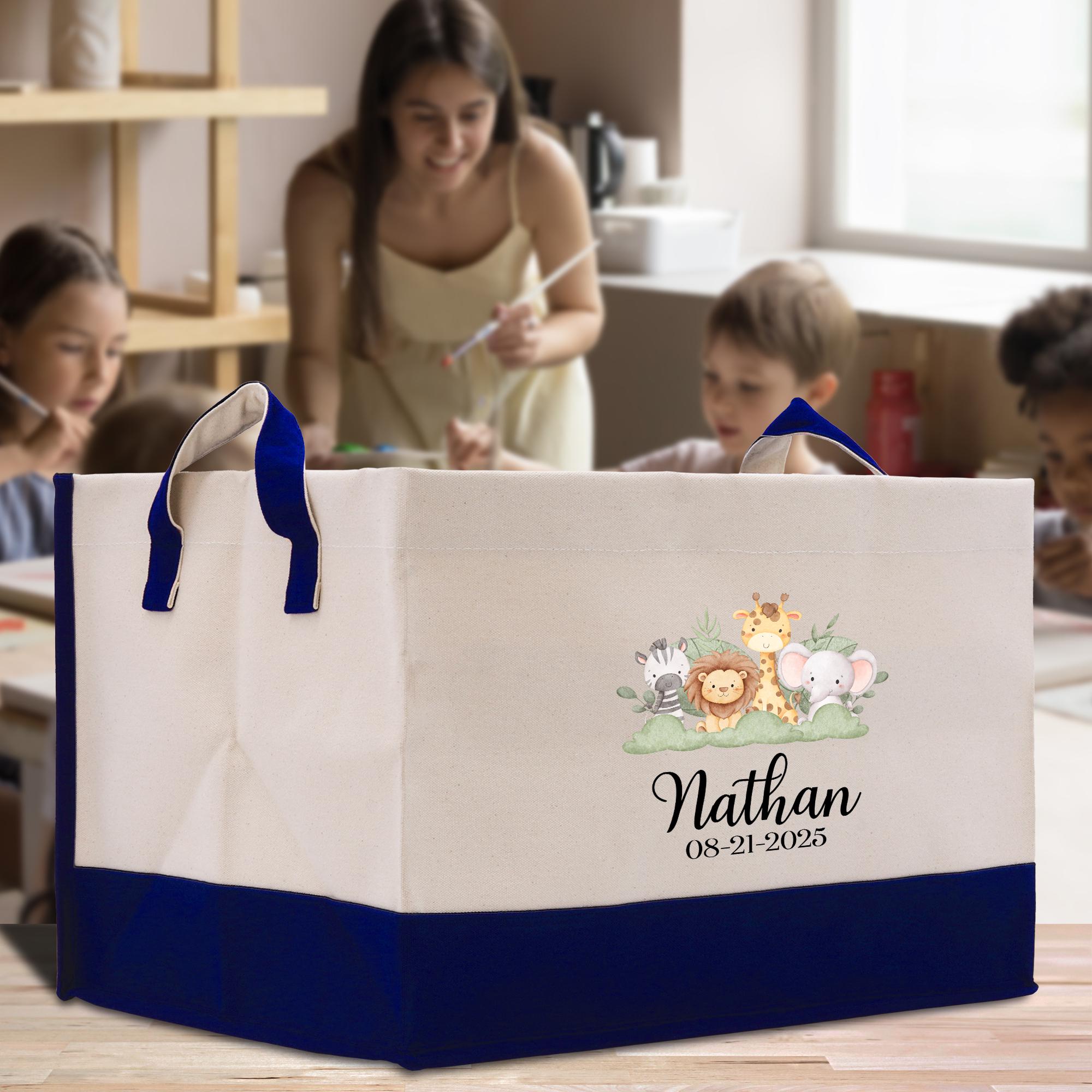 A large white tote bag with a blue handle, featuring a cartoon illustration of various animals and the name &quot;Nathan&quot; printed on it. The bag is placed on a table, and there are people in the background, suggesting it might be a gift or a personal item.