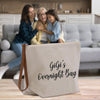 two women sitting on a couch with a bag in front of them