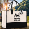 A white tote bag with a black and white graphic design and text printed on it, placed on a wooden surface with a natural outdoor background.