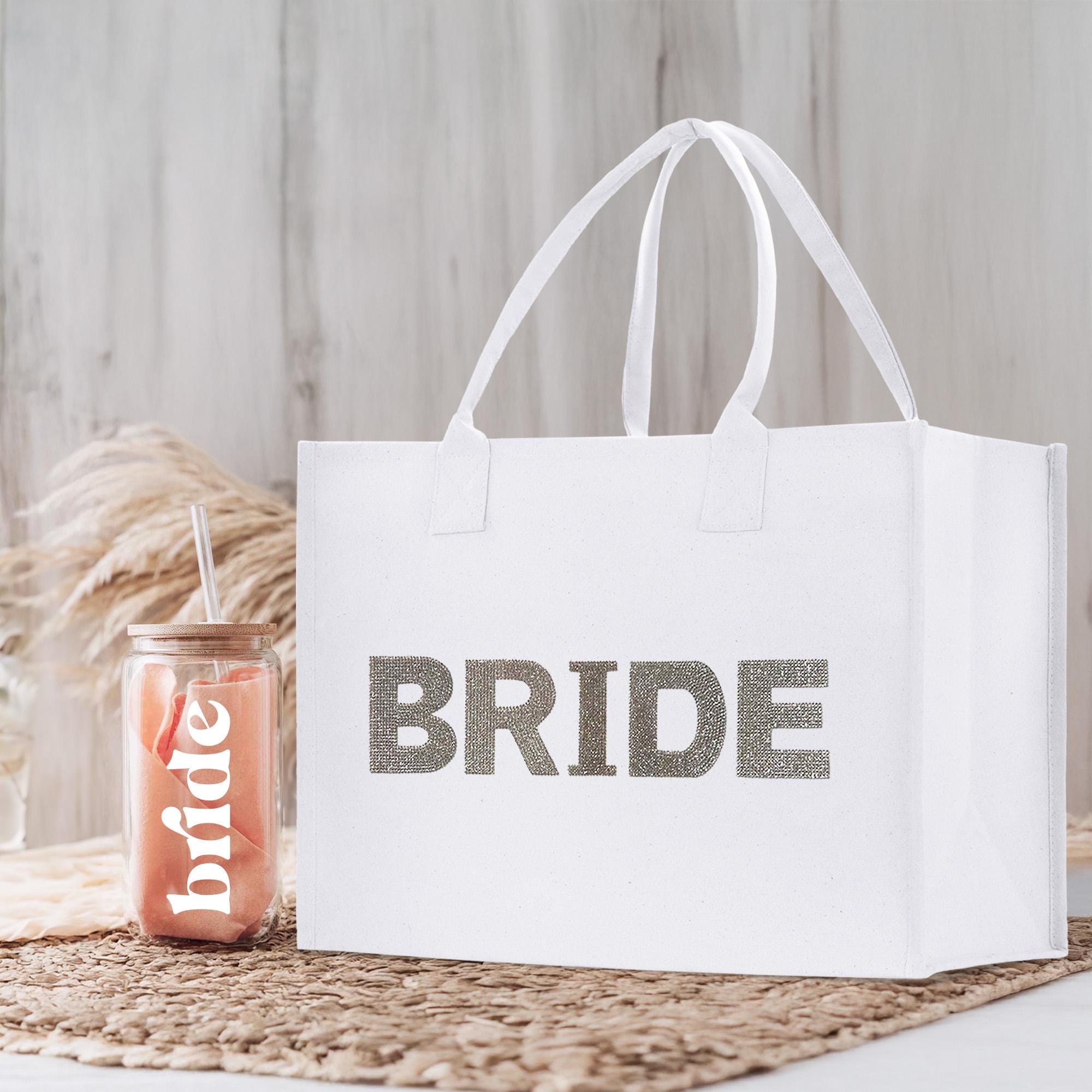 A white tote bag with the word &quot;BRIDE&quot; printed on it, placed next to a glass jar with a straw.