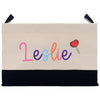 A beige canvas bag with the name "Leslie" printed on it in colorful cursive letters. There is also a small heart-shaped lollipop icon on the bag.