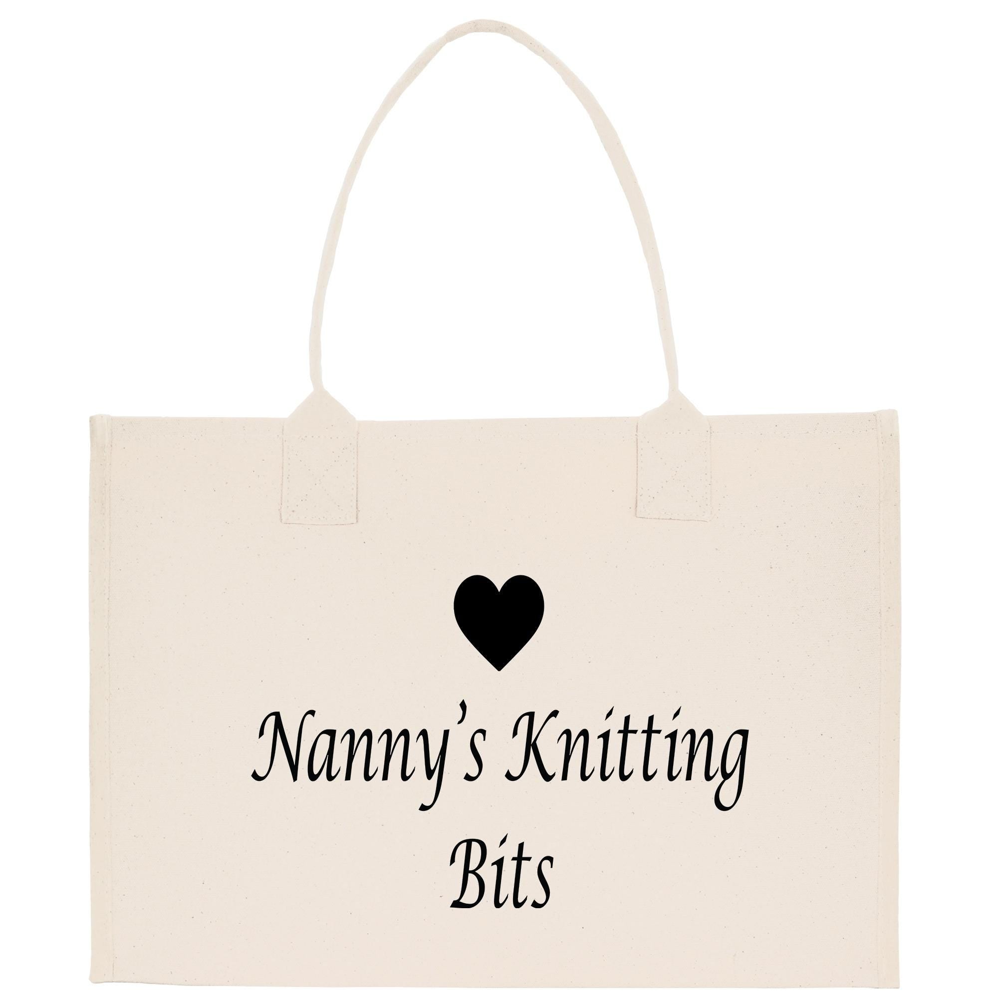 A beige tote bag with the text &quot;Nanny&#39;s Knitting Bits&quot; printed on it, along with a small black heart symbol.