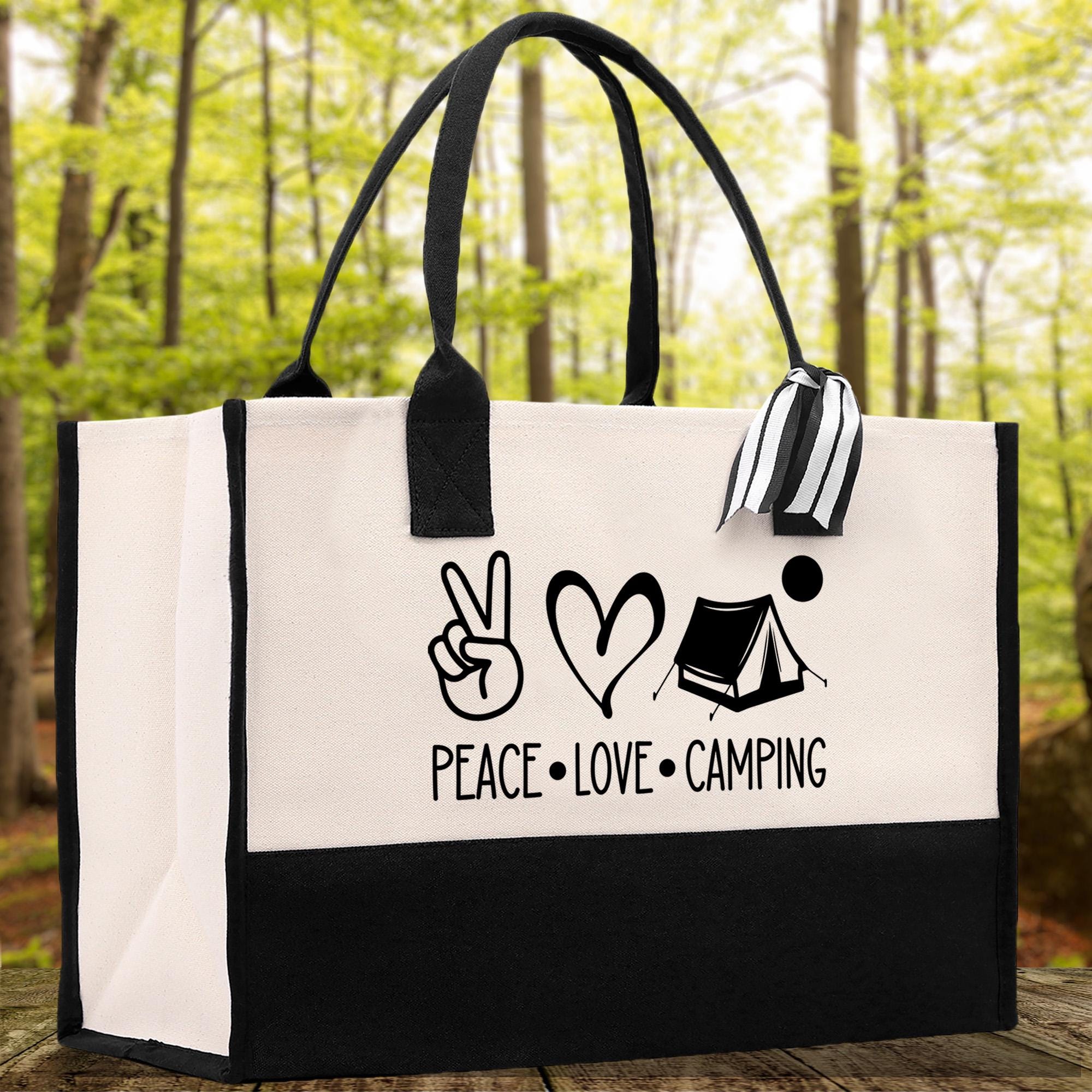 A black and white tote bag with a printed design on it, featuring the words "PEACE LOVE CAMPING" and a peace sign, a heart, and a tent.