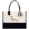 A beige tote bag with a black handle and a black and white striped ribbon tied around it. The bag has a floral design on the front and the word "Marley" printed on it.