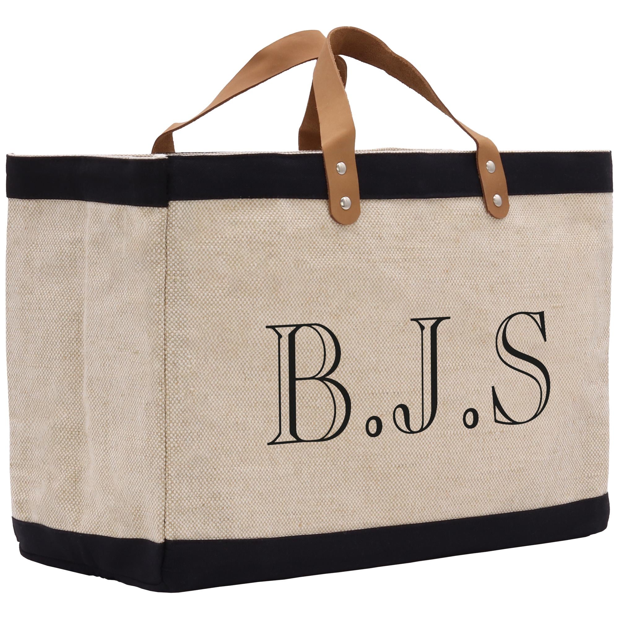 A beige tote bag with black trim and leather handles, featuring the initials &quot;B.J.S.&quot; printed on it.