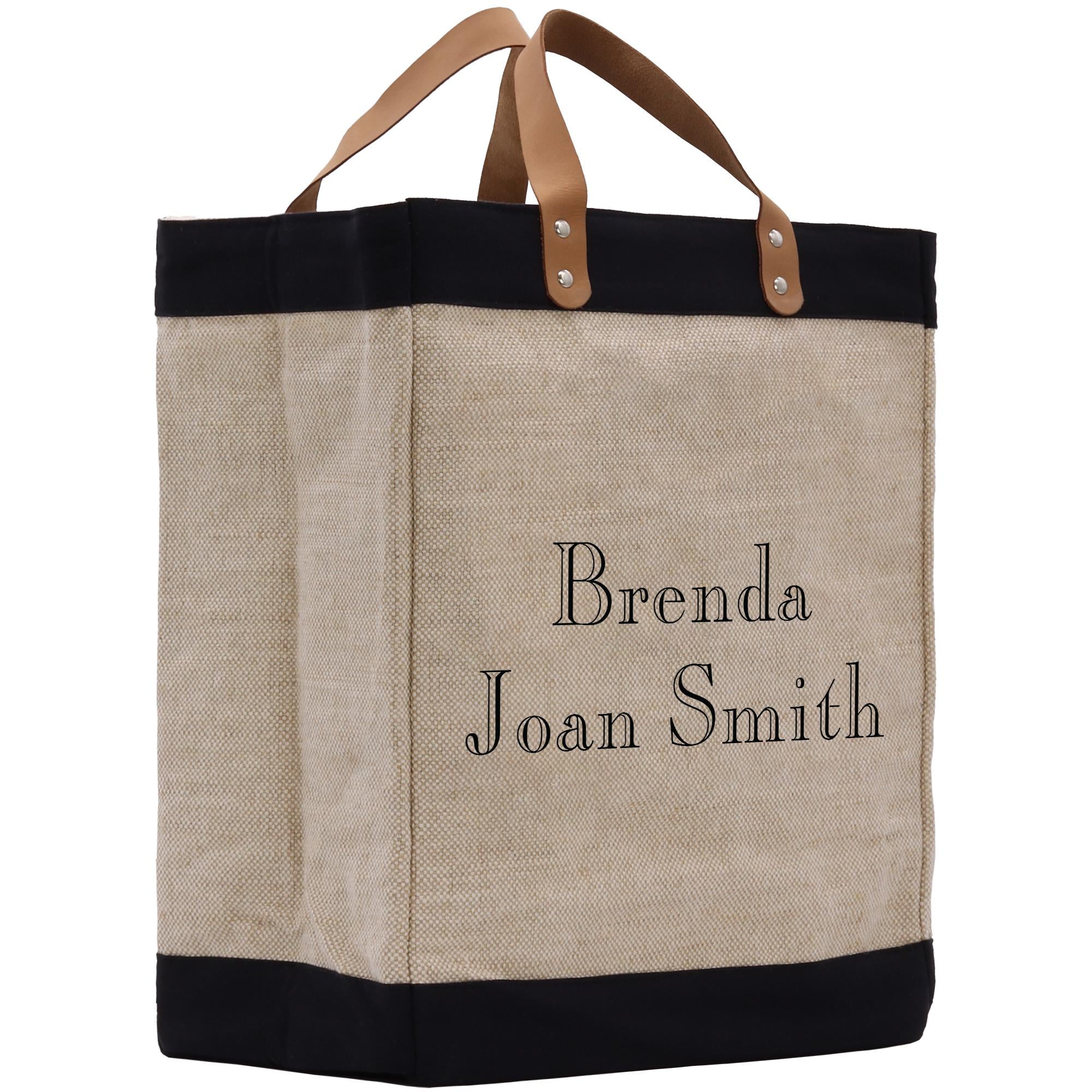 A beige tote bag with black trim and leather handles, featuring personalized text on the front.