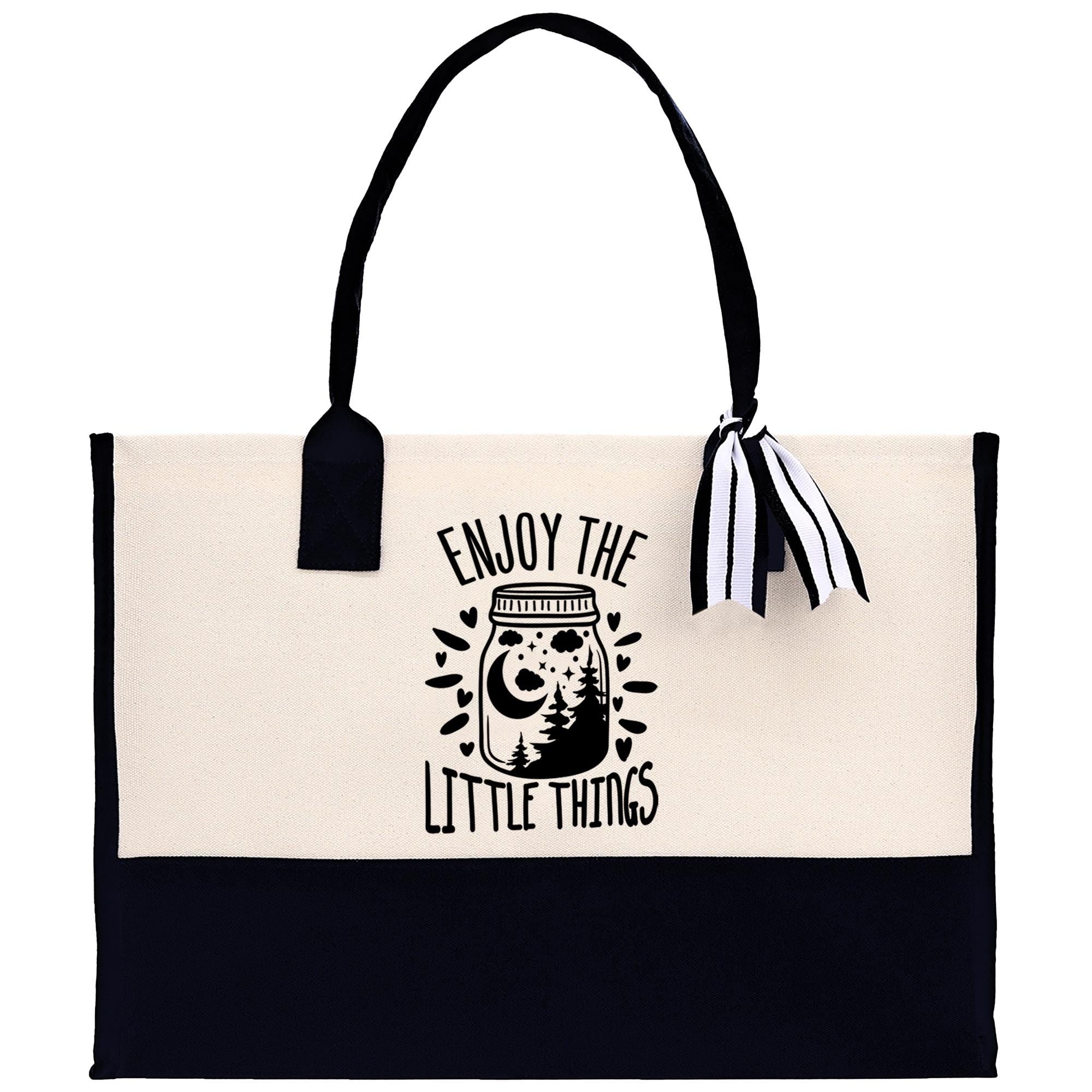 A tote bag with a black and white design featuring a jar with a crescent moon and stars, along with the text "Enjoy the little things" printed on it.