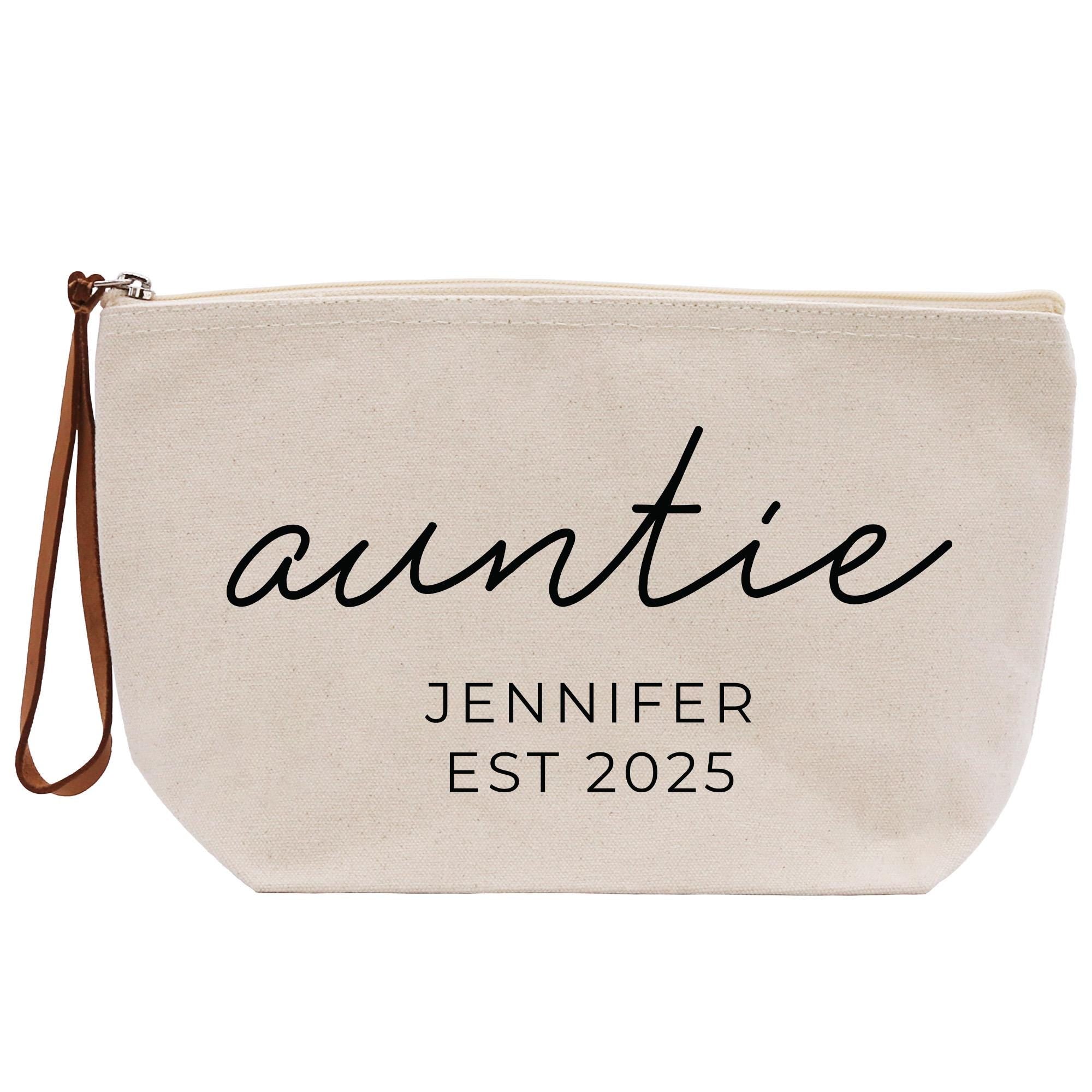 A beige canvas tote bag with the text &quot;auntie&quot; and &quot;JENIFER EST 2025&quot; printed on it.