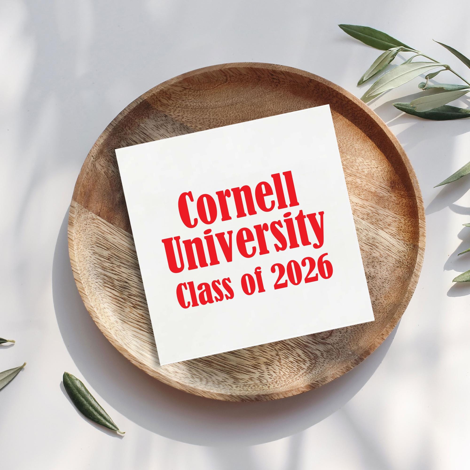 A white paper with red text is placed on a wooden plate, surrounded by green leaves.
