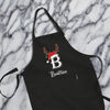 A black apron with a personalized monogrammed name and a Santa hat on it, placed on a marble surface.
