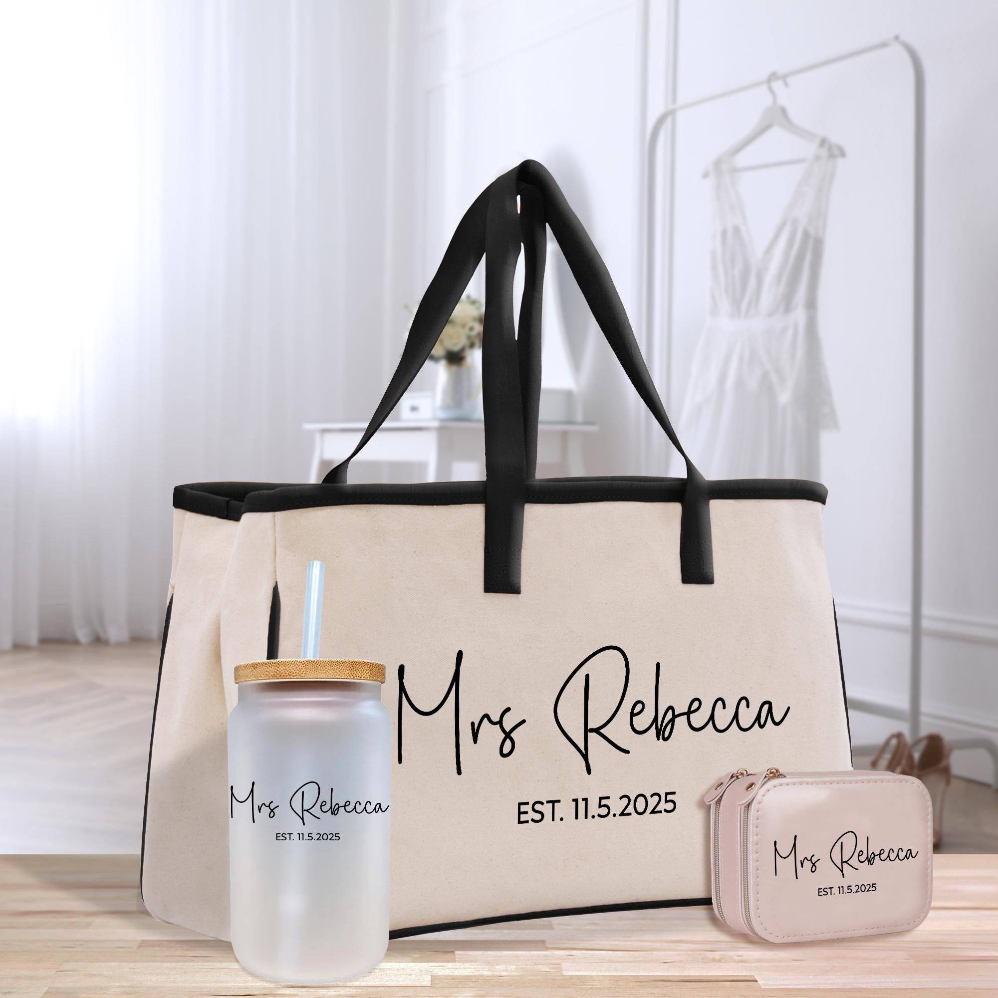 A beige tote bag with the name &quot;Mrs Rebecca&quot; printed on it, along with a matching drink cup and a small purse, all placed on a wooden surface.