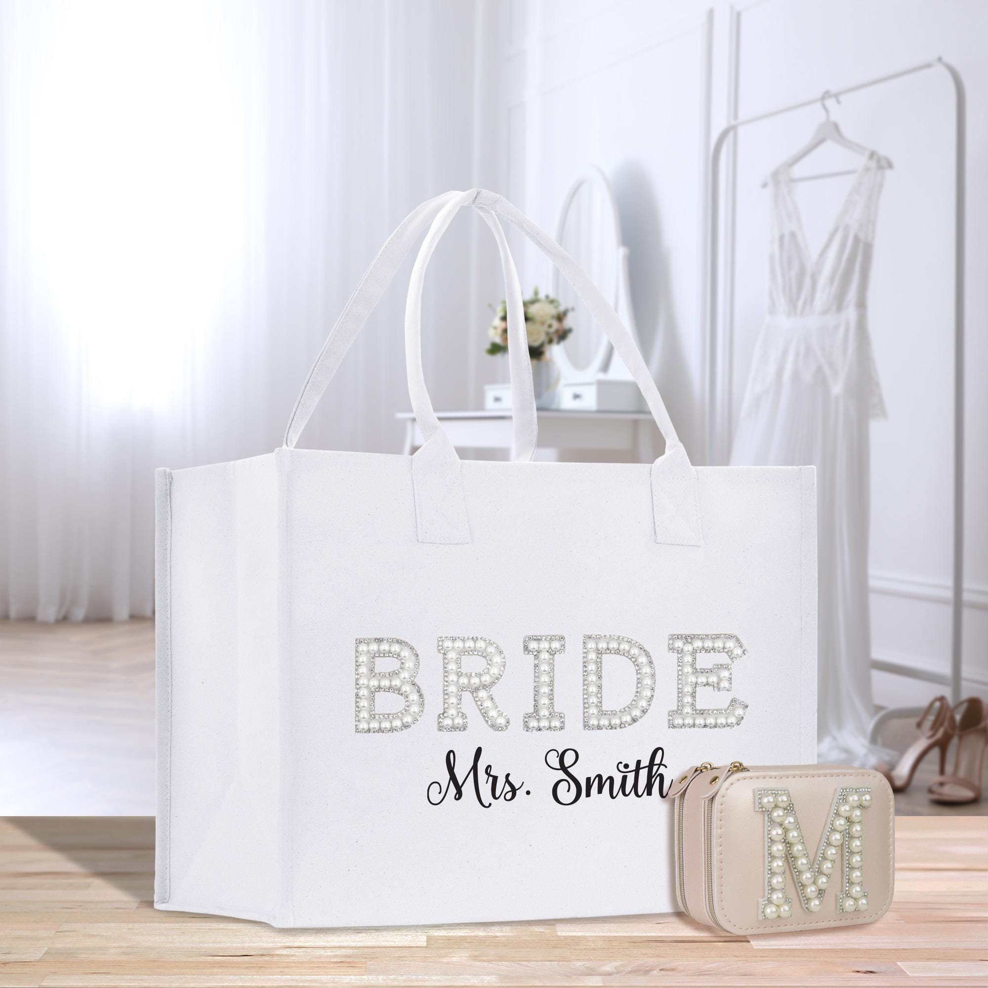 A white tote bag with the text &quot;BRIDE Mrs. Smith&quot; printed on it, along with a matching purse and a dress in the background.