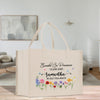 A beige tote bag with a floral design and text printed on it, placed on a wooden surface in a room with a painting hanging on the wall.
