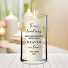 A white candle with a message written on it, placed in a glass vase on a wooden surface.
