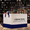 A white and blue bag filled with various books, placed on a wooden surface in front of a bookshelf.