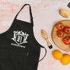 A black apron with a white coat of arms and the name "ROBERTSON" printed on it, along with a wooden juicer and a plate of fresh fruits, including oranges and tomatoes.