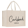 A beige canvas tote bag with the text "Carlsbad California" printed on it.