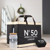 a black tote bag with the text "N°50 Rebecca Smith London" printed on it, along with a matching black and white glass jar with a straw and a small black box with the same text "N°50 Rebecca Smith London" printed on it.
