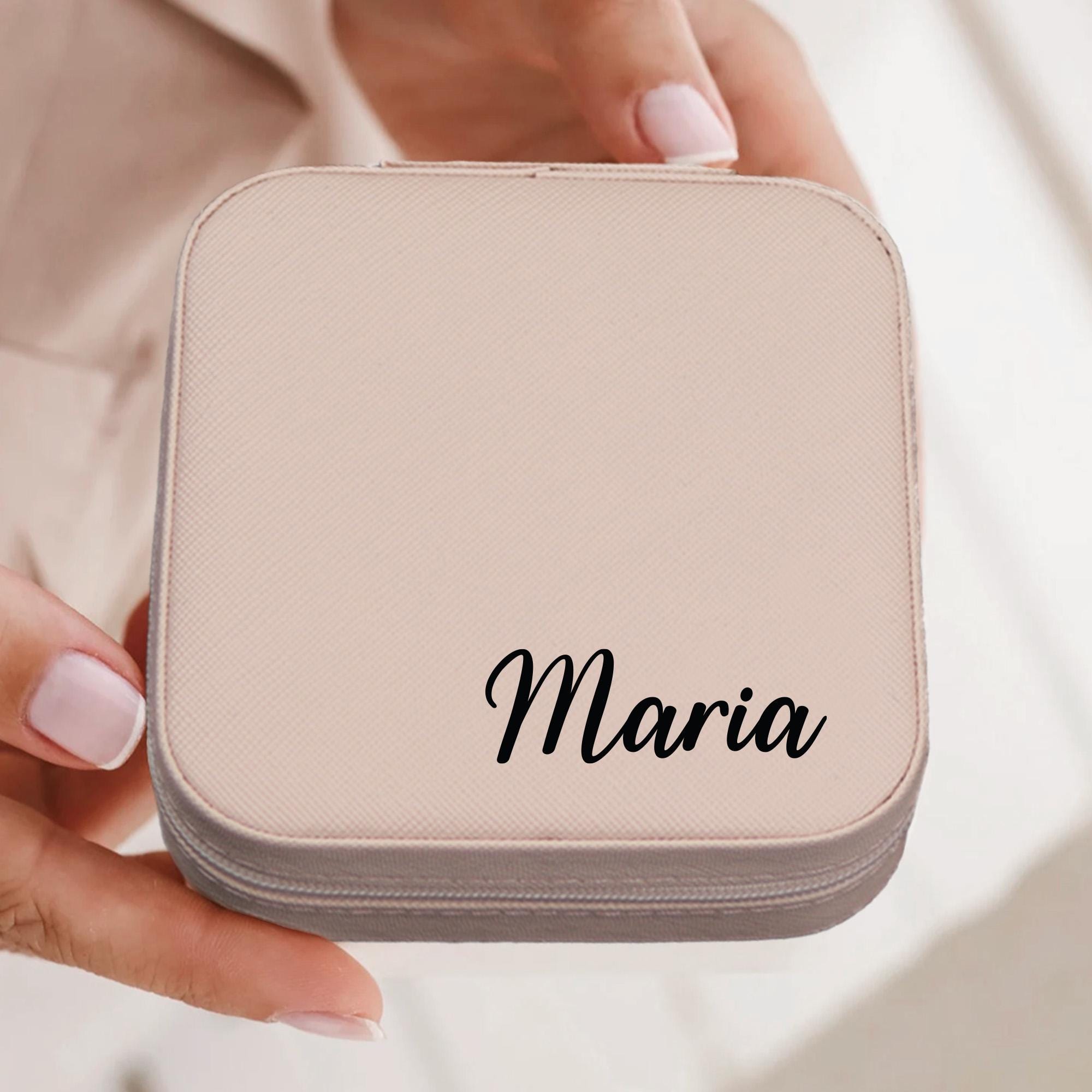 A person&#39;s hand holding a small, square-shaped case with the name &quot;Maria&quot; printed on it.