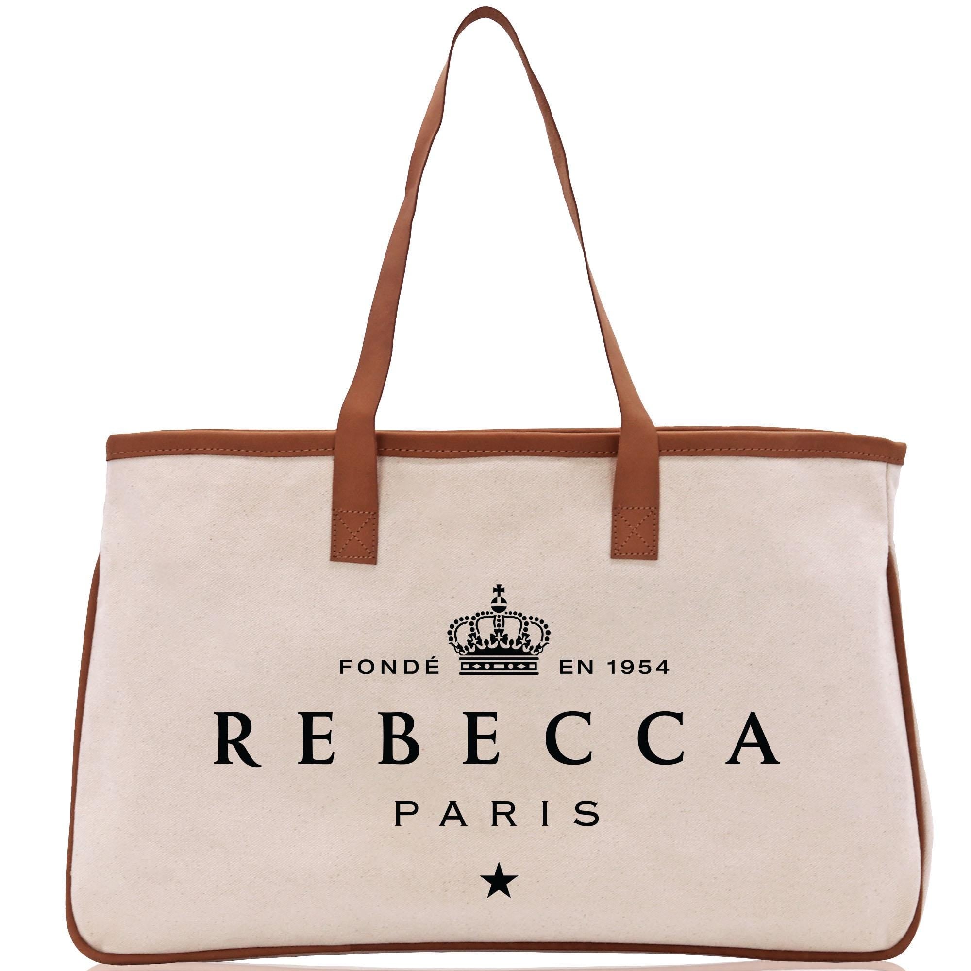 A tan tote bag with a brown leather strap and the text &quot;REBECCA PARIS&quot; printed on it.