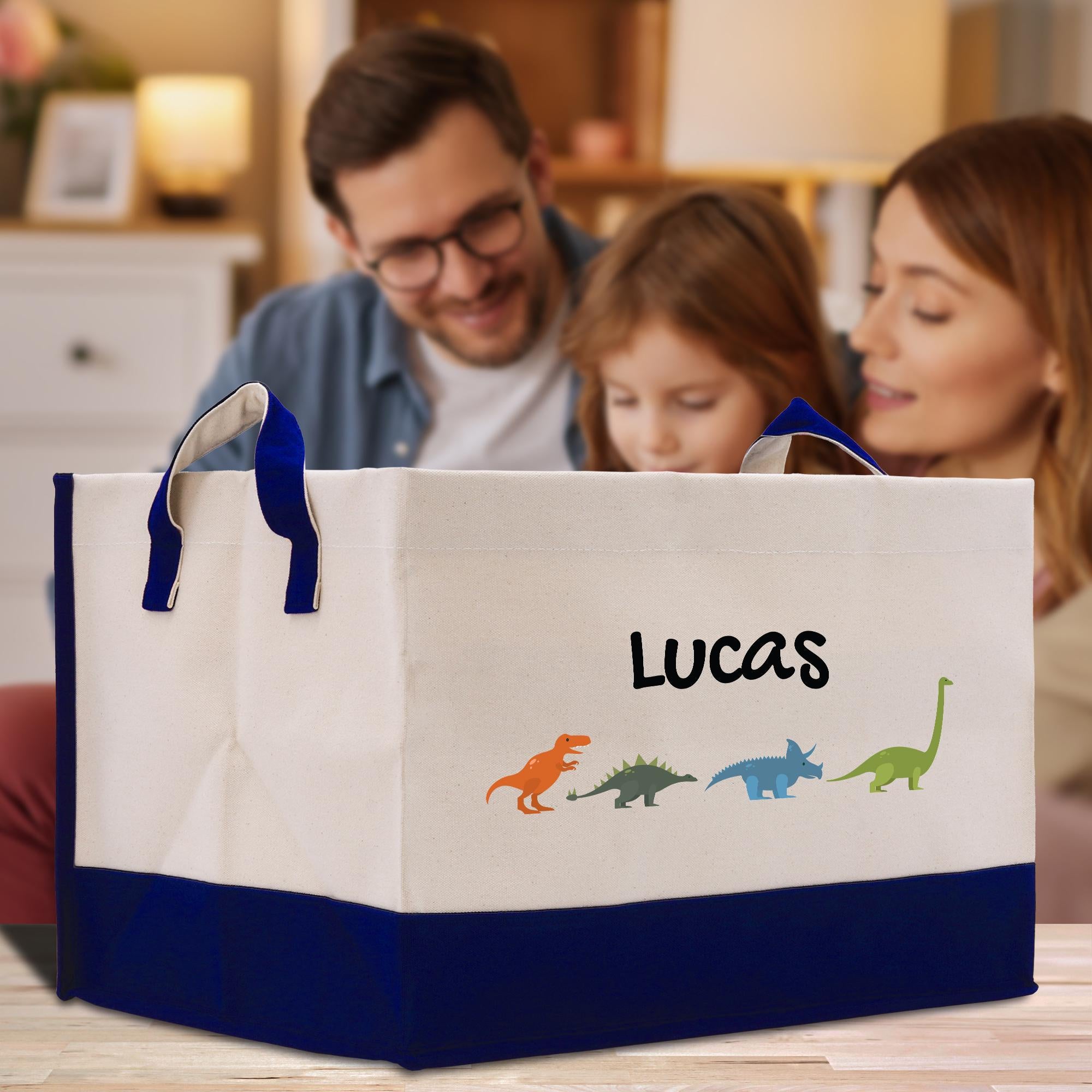 A family of three, including a man, a woman, and a young girl, are gathered around a large storage bin with a dinosaur design and the name &quot;Lucas&quot; printed on it.