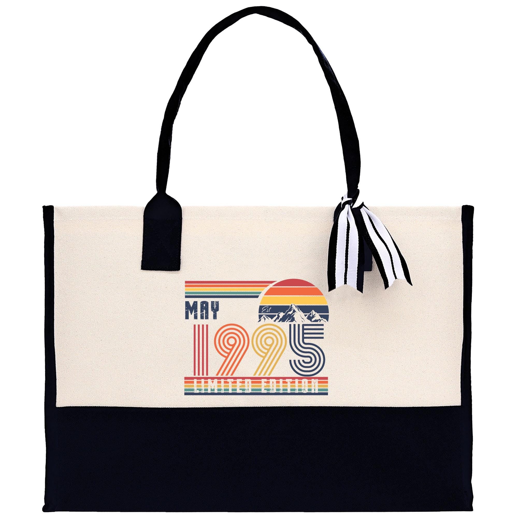 A beige tote bag with a black handle and a black and white striped ribbon attached to it. The bag has a graphic on the front that says "MAY 1995 LIMITED EDITION".