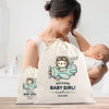A woman holding a baby, with a large white bag featuring a cartoon airplane and the text "Welcome Baby Girl! Sophia 04.02.2025" in the foreground.