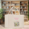 A beige tote bag with a floral design and the text "Rachel's Version" printed on it, placed on a wooden surface.