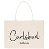 A beige canvas tote bag with the text "Carlsbad, California" printed on it.