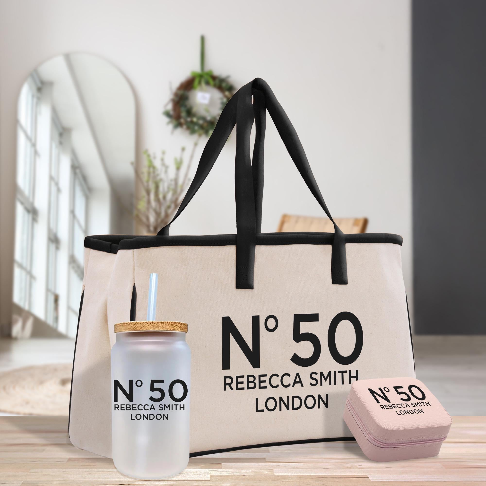 A beige tote bag with the text &quot;N°50 Rebecca Smith London&quot; printed on it, along with a clear jar with a straw and a small pink container.