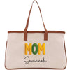 A beige canvas tote bag with the word "MOM" printed in large yellow letters and the name "Savannah" written in smaller black letters below.