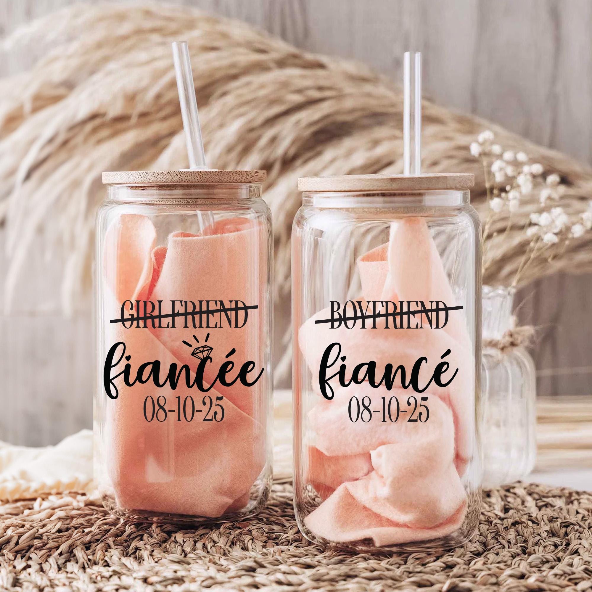 Two glass jars with straws, each containing a pink fabric item, labeled with the text &quot;GIRLFRIEND fiancee 08-10-25&quot; and &quot;BOYFRIEND fiancee 08-10-25&quot; respectively.