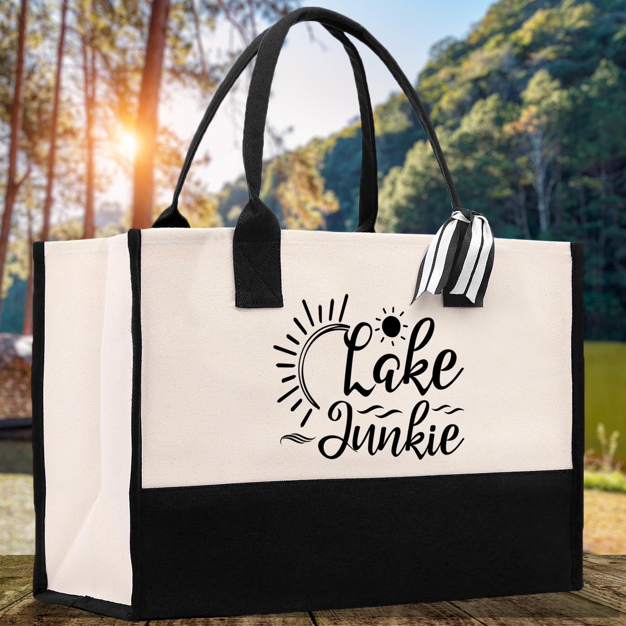 A black and white tote bag with the text "Lake Junkie" printed on it, placed on a wooden surface with a natural outdoor background.