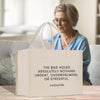 A white tote bag with text printed on it, placed on a wooden surface. In the background, there is a person sitting on a couch.