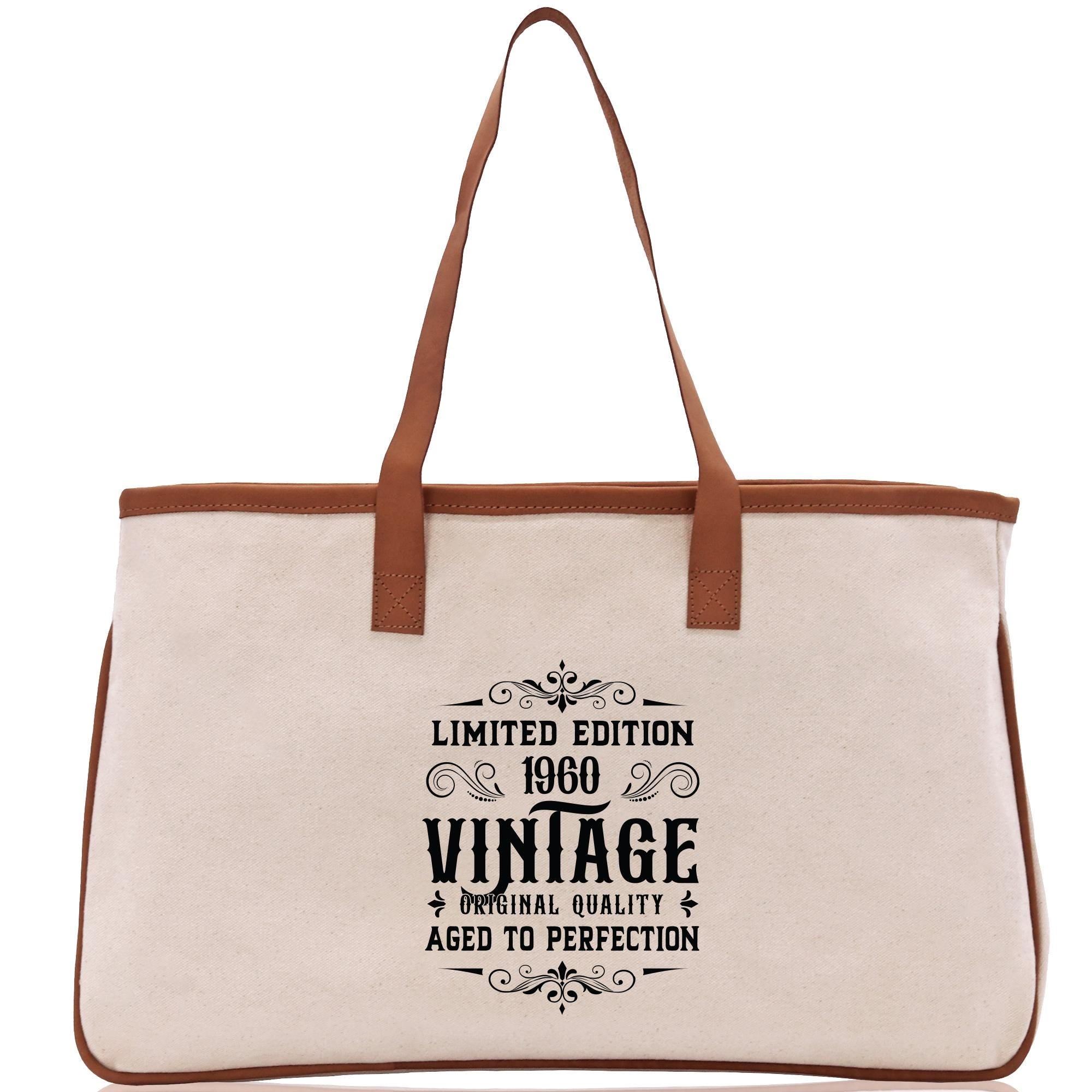 A beige canvas tote bag with a brown leather strap and a printed design on the front that reads "LIMITED EDITION 1960 VINAGE ORIGINAL QUALITY AGED TO PERFECTION".