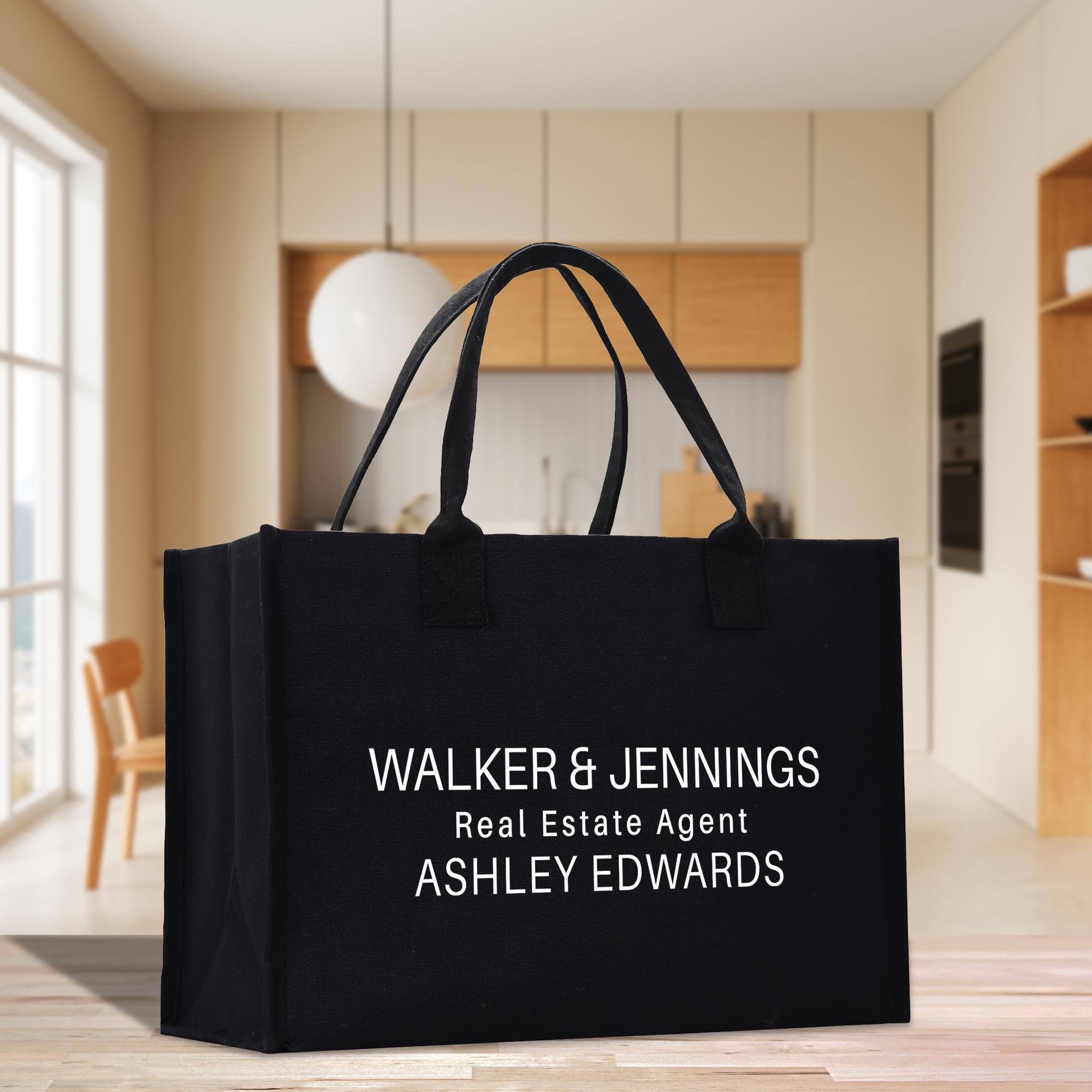 A black tote bag with white text on it, placed on a wooden floor in a modern-looking room with a window and wooden furniture.