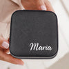 A person's hand holding a black, square-shaped case with the name "Maria" written on it in white text.