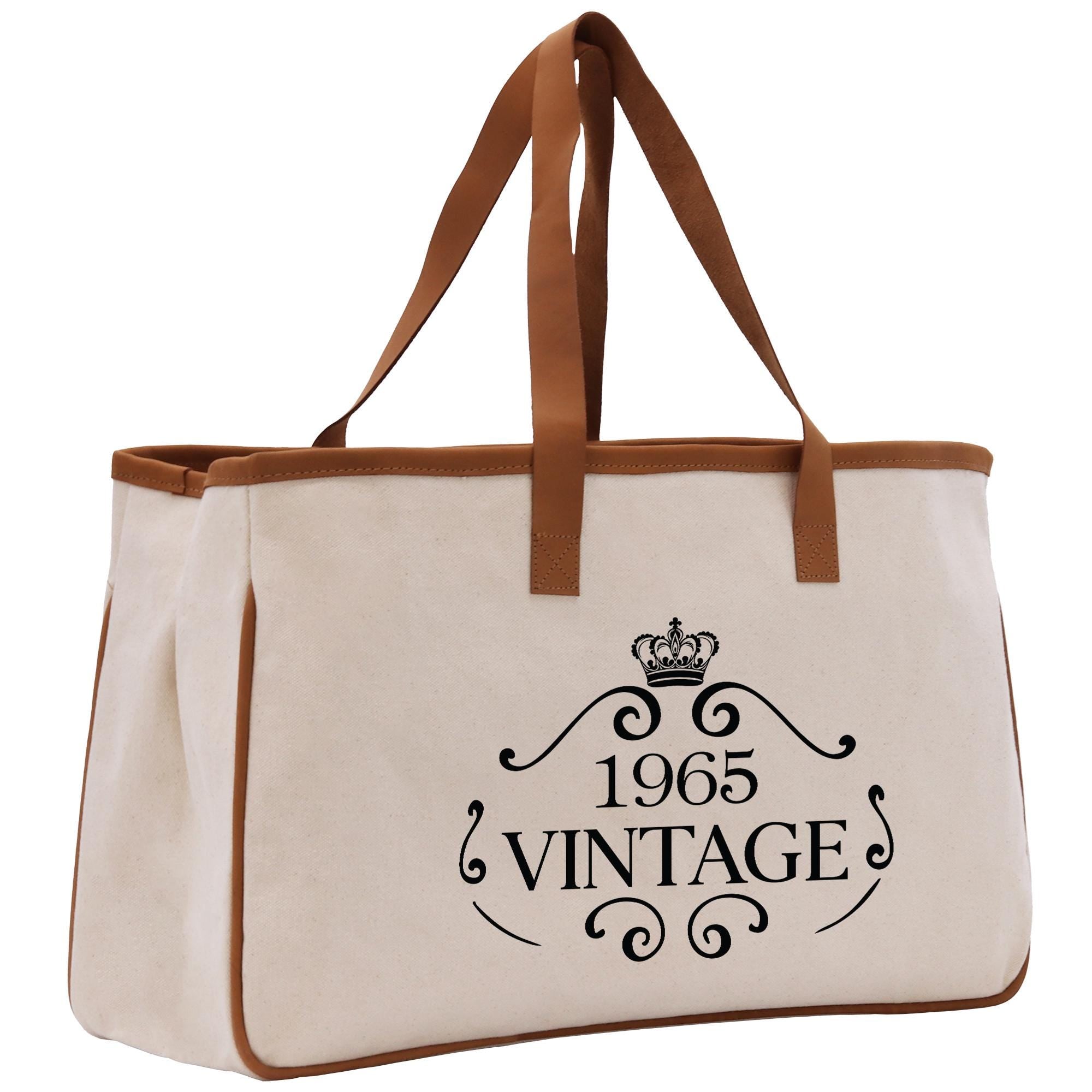A beige canvas tote bag with a brown handle and a crown design, printed with the text "1965 VINTAGE".