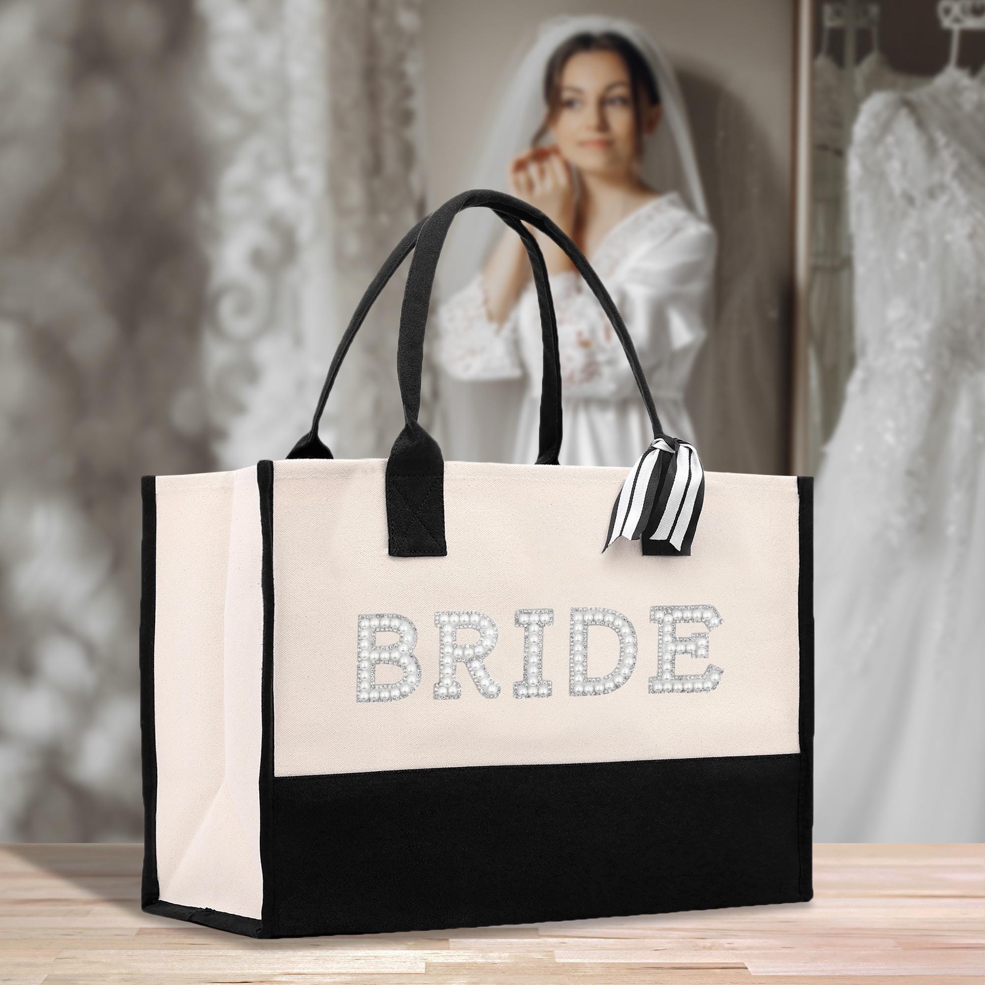 A black and white tote bag with the word &quot;BRIDE&quot; printed on it, placed on a wooden surface. In the background, there is a blurred image of a woman wearing a white wedding dress.