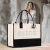 A black and white tote bag with the word "BRIDE" printed on it, placed on a wooden surface. In the background, there is a blurred image of a woman wearing a white wedding dress.