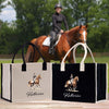 A woman is riding a brown horse in a field, with two bags featuring a horse image and the name "Katherine" printed on them.