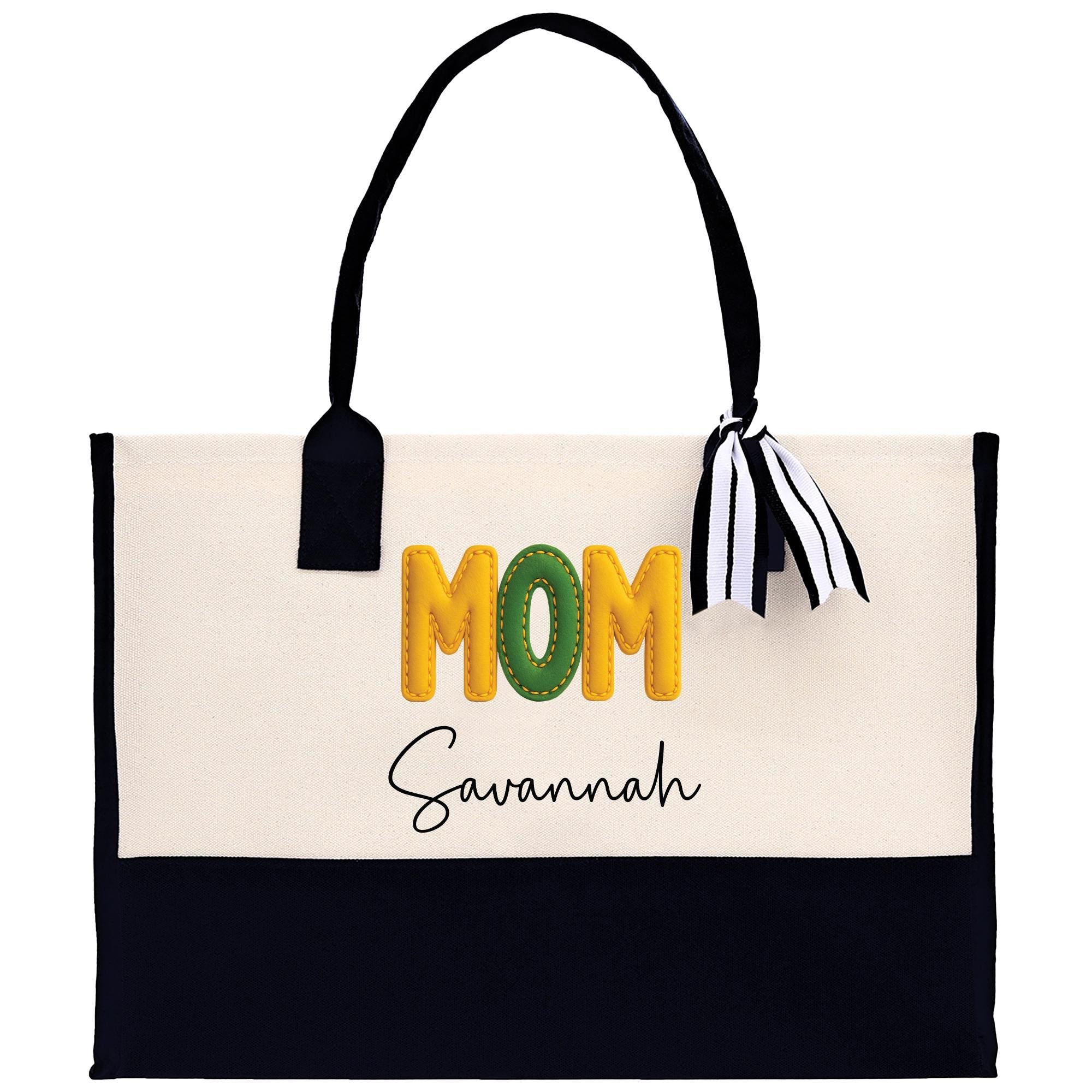 A beige tote bag with the word &quot;MOM&quot; printed in large letters, along with the name &quot;Savannah&quot; written below it. The bag has a black handle and a black and white striped ribbon tied around it.