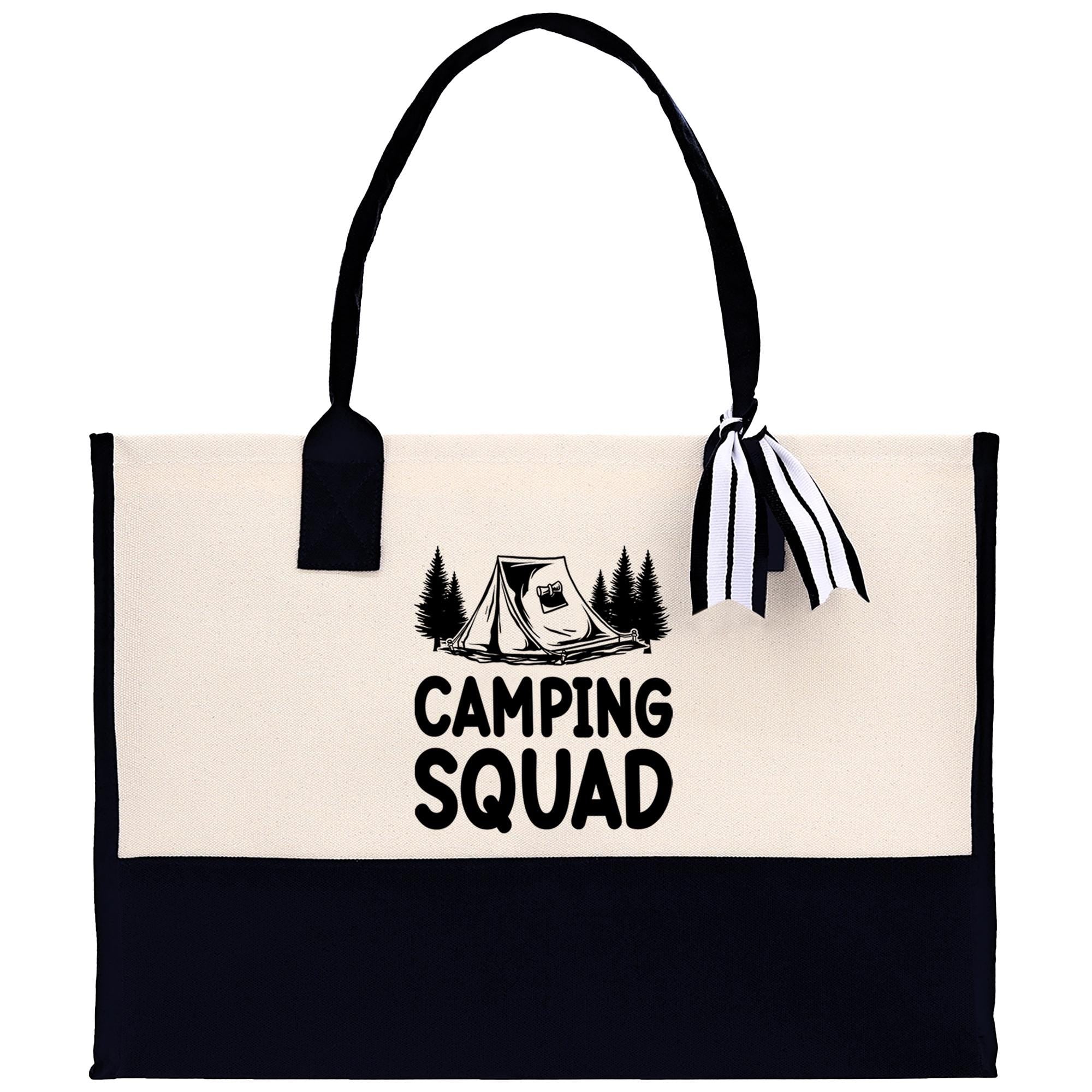 A beige canvas tote bag with a black handle and a black and white striped ribbon attached to it. The bag has a graphic of a tent and trees printed on it, along with the text "CAMPING SQUAD" printed on it.