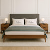 A modern bedroom with a large bed, wooden headboard, and two nightstands with lamps. The bed has two pillows with the names "Mr. Jones" and "Mrs. Jones" printed on them.