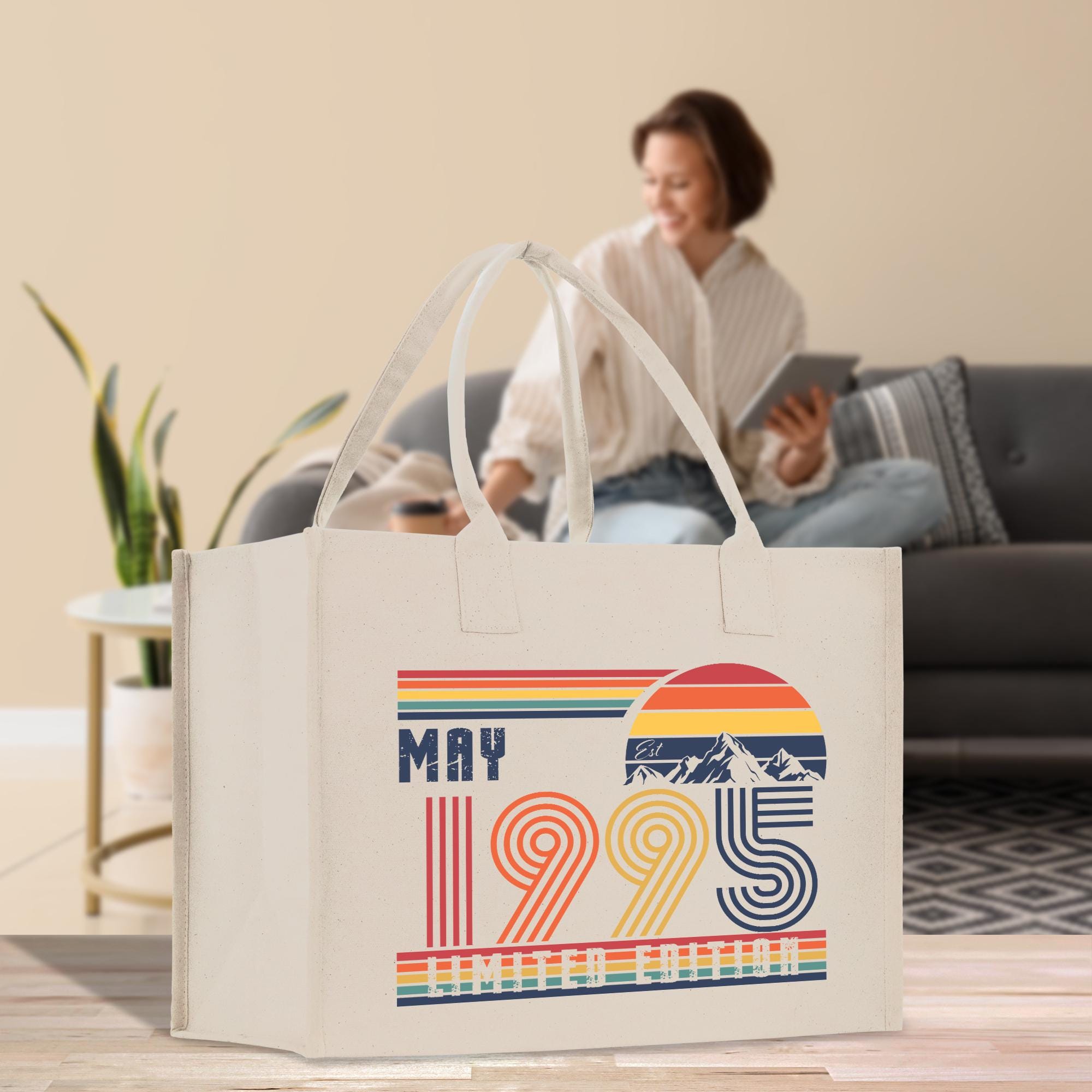 A white tote bag with a graphic design featuring a woman and mountains, along with the text "MAY 1995" and "CHILDREN EDITION".