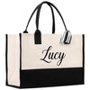A large tote bag with a black and white color scheme. The bag has a name tag attached to it, and the name "Lucy" is printed on the front in a cursive font.