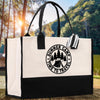 A white tote bag with a black and white graphic design featuring a camping scene and the text 