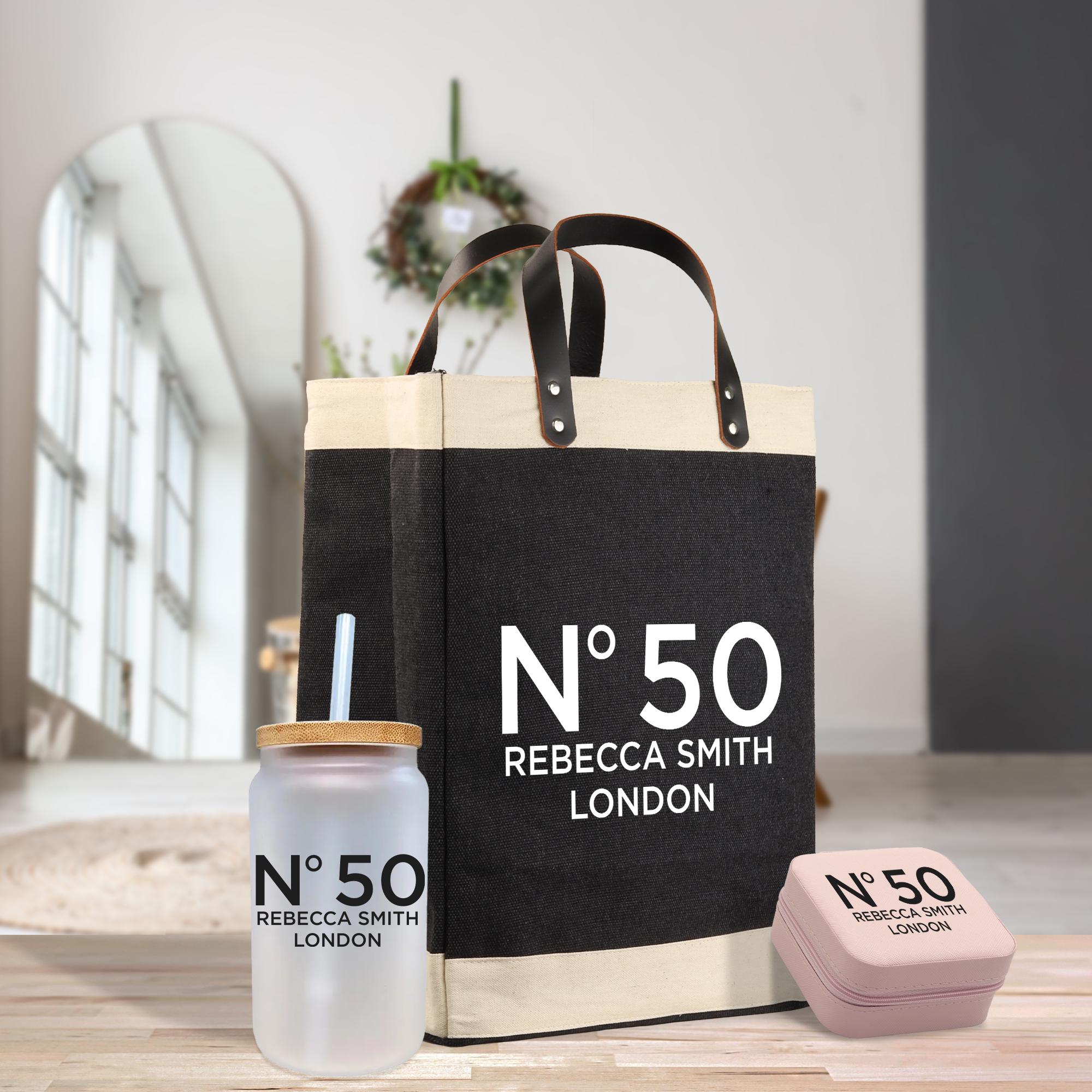 a black and white tote bag with the text "N°50 Rebecca Smith London" printed on it, along with a matching black and white jar with a straw and a pink box with the same text "N°50 Rebecca Smith London" printed on it.