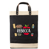 A black tote bag with a beige trim, featuring a personalized name printed on it. The bag also has various school-related items such as a pencil, an apple, and a ruler printed on it.