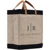 A beige tote bag with a black trim and leather handles, featuring the logo and text "Jil'l Rae Designs" printed on it.